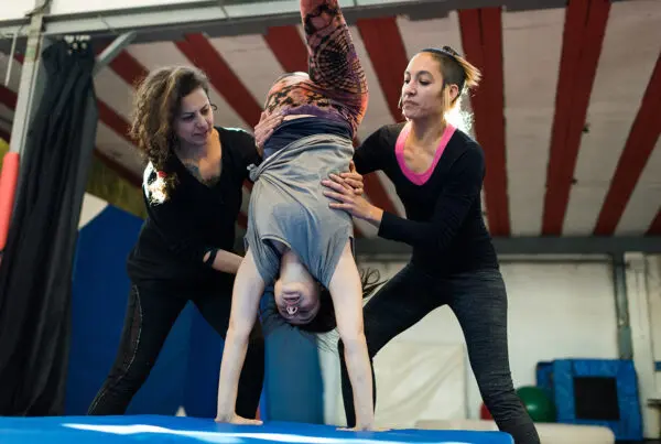 Two women helping girl to do handstand in gymnasium