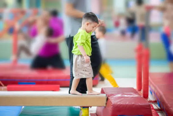 Gymnastics for kids: Toddler boy being helped by coach to learn beam walk