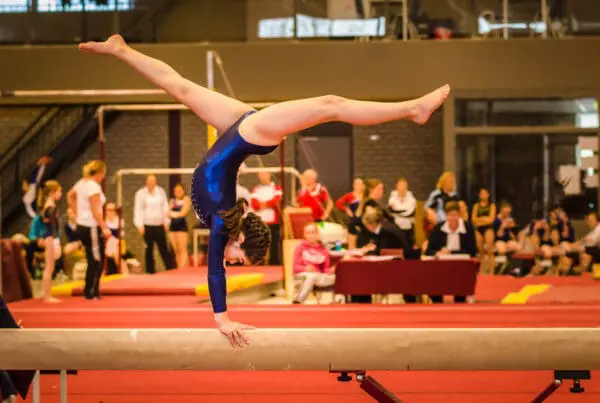 A young gymnast girl within the compulsory gymnastics levels practicing for a competition by performing a choreographed routine on a balance beam.