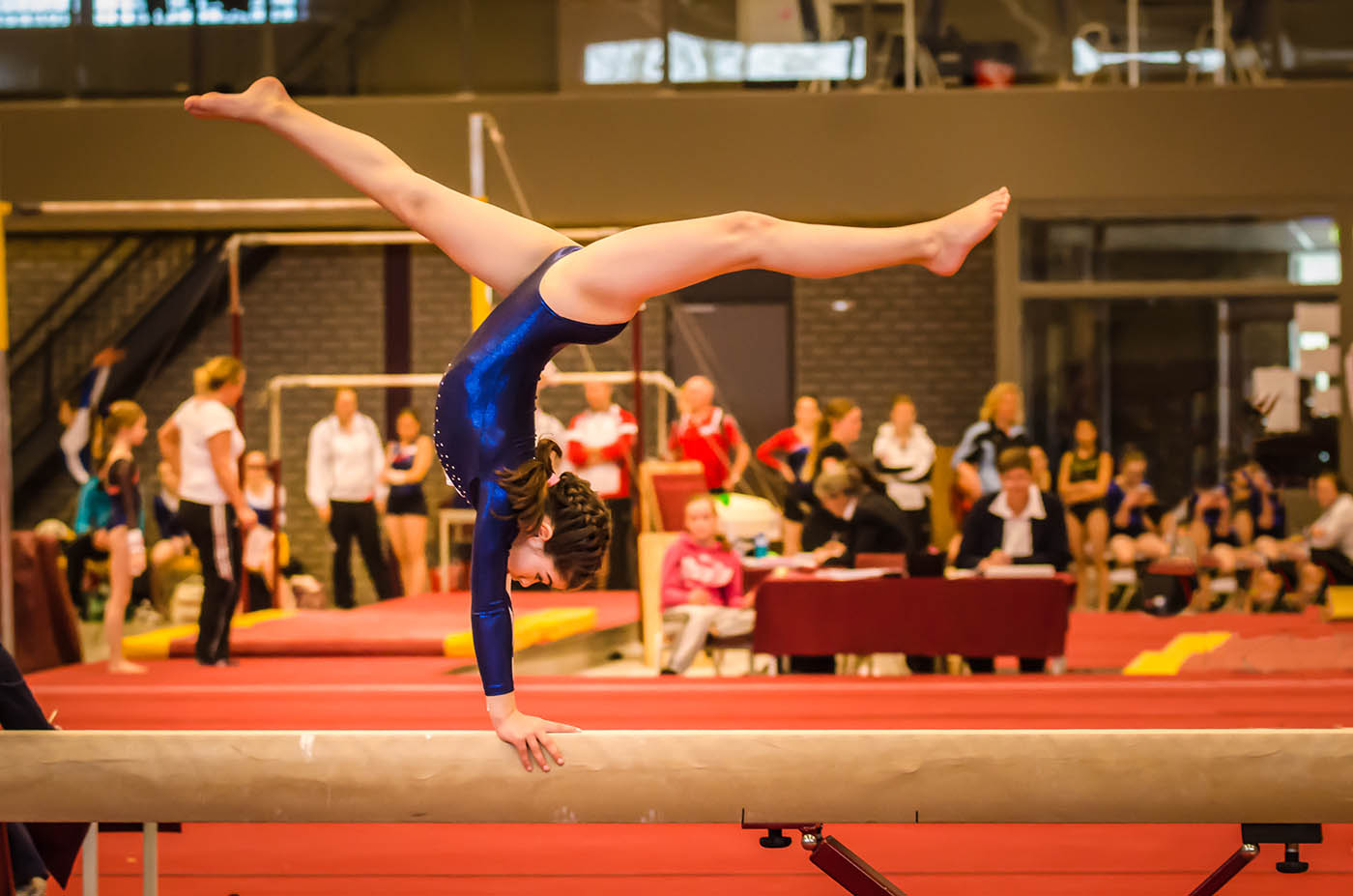 A young gymnast girl within the compulsory gymnastics levels practicing for a competition by performing a choreographed routine on a balance beam.
